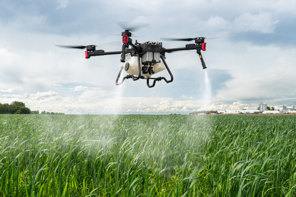 An agricultural drone set against a backdrop of blue skies and green fields where crops are growing.